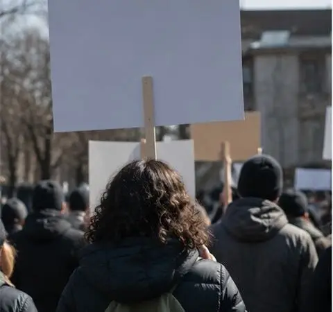 Demonstrators hold placards at an outdoor rally, seen from behind.